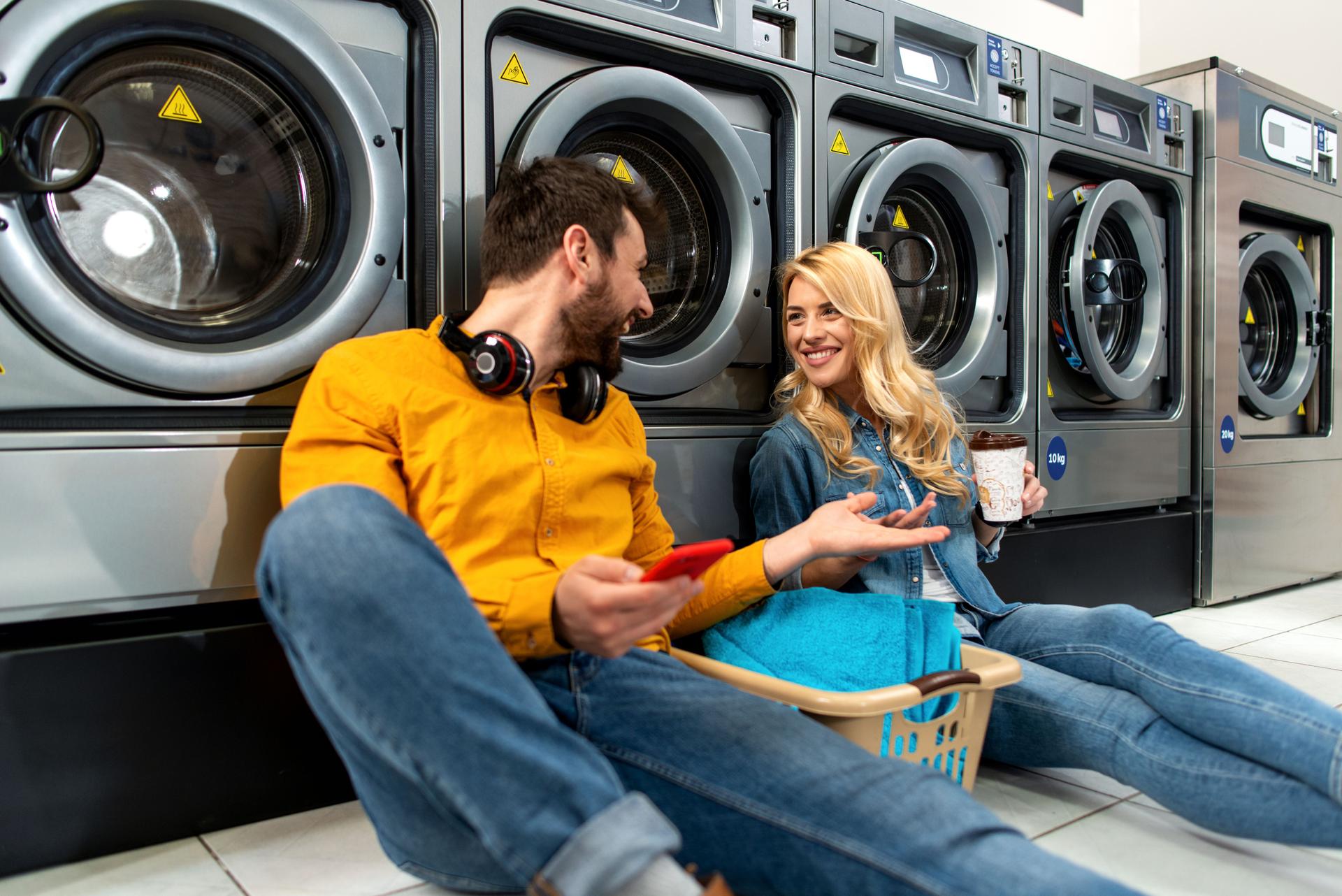 Young cheerful couple doing laundry together at laundromat shop.